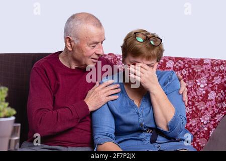 Ein alter Mann tröstet seine Frau, die auf dem Sofa sitzt. Seniorenpaar zu Hause. Stockfoto