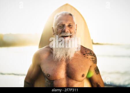 Fit Senior männlich Spaß beim Surfen während Sonnenuntergang - Pensionierter Mann, der am Strand mit Surfbrett trainiert Stockfoto