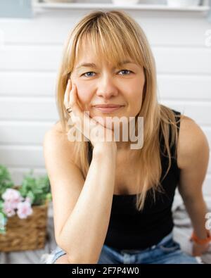 Nahaufnahme Porträt der Blondine, mit Pony, Landschaft Designerin Frau 40-42 Jahre alt, blickt in die Kamera, Hand unter dem Kinn, ohne Make-up. Lächeln auf fa Stockfoto