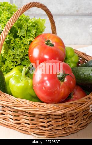 Frisches Gemüse, bedeckt mit Wassertropfen in einem braunen Korb. Große Bio-Tomaten, Gurken, grüner Pfeffer und lebhafter grüner Salat vom Markt. F Stockfoto