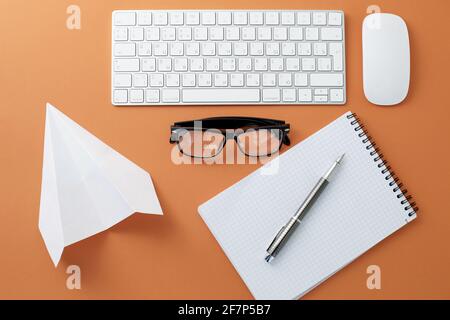 Brille weiß Tastatur Maus Notizblock und Papier Ebene auf orange Hintergrund Stockfoto