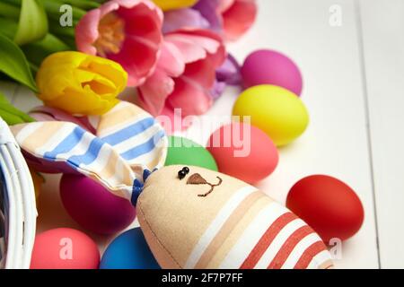 Osterhase Puppe und Ostereier und Frühling bunte Blumen auf weißem Holztisch. Bemalte Hühnereier und bunte Tulpen, Einrichtung am Ostertag, s Stockfoto