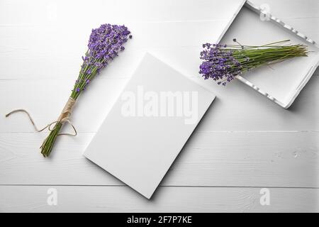 Weißes Canvas-Mockup und Lavendelblüten-Bouquet im Tablett auf weißem Holztisch-Hintergrund, flach liegend. Leere Leinwand, Draufsicht Stockfoto