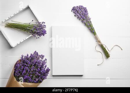 Weißes Canvas-Mockup und Lavendelblüten-Bouquet im Tablett auf weißem Holztisch-Hintergrund, flach liegend. Leere Leinwand, Draufsicht Stockfoto