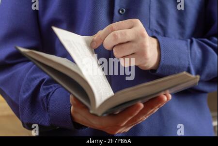 Ein junger Mann, ein Schuljunge oder ein Student hält ein offenes Buch in seinen Händen und dreht die Seite um Stockfoto