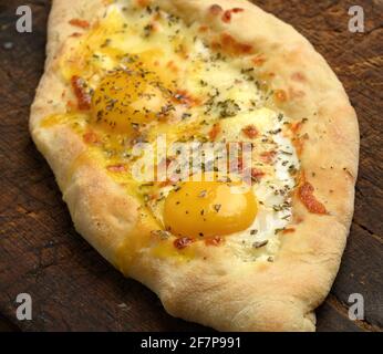 Gebackene Adjarian-Khachapuri mit dem ganzen Eigelb auf Holzbrett, traditionelles Gericht Stockfoto