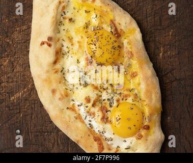 Gebackene Adjarian-Khachapuri mit dem ganzen Eigelb auf Holzbrett, traditionelles Gericht Stockfoto