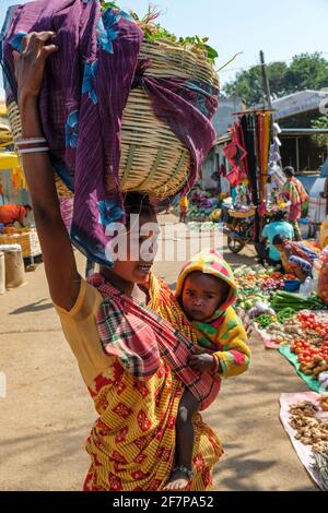 Koraput, Indien - 2021. Februar: Adivasi-Frau aus dem Stamm Kondh mit ihrem Kind beim Gemüseeinkauf auf dem Koraput-Markt am 21. Februar 2021 in OD Stockfoto