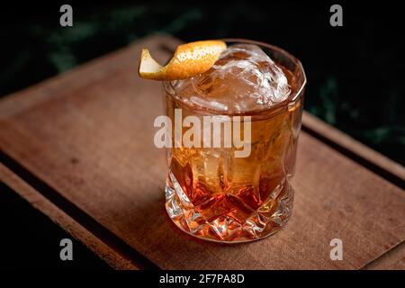 Ein altmodischer, klassischer Cocktail, der mit einem Eisball in einem schönen Steinglas serviert wird, mit einer Orangenschale als Garnierung. Stockfoto