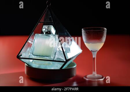 Ein wirklich schöner Cocktail, der in einer parfum-Flasche auf Eis in einer transparenten, diamantförmigen Schachtel mit einem Nick- und Nora-Glas serviert wird Stockfoto