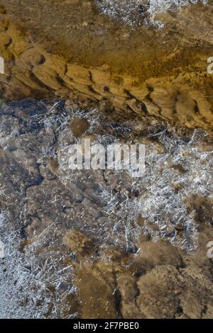 Frühlingsmuster aus sandigem Bachboden und durchscheinender Eiskruste Nahaufnahme Stockfoto