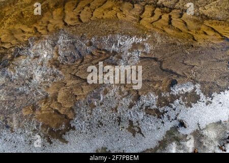 Kurve der gemusterten Streambed und der Eiskruste an Der Rand der Strömung an einem Frühlingsmorgen Stockfoto
