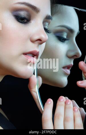 Mädchen mit einem Schard des Spiegels. Weibchen mit Spiegelschard in der Hand, die auf grauem Hintergrund posiert. Gesichtsreflexion im Spiegelsplitter. Stockfoto