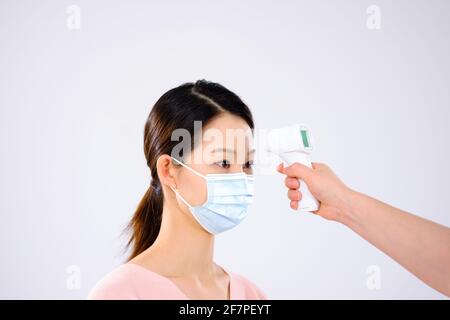 Eine junge Dame mit einer Maske nahm ihre Temperaturseite ein Anzeigen Stockfoto