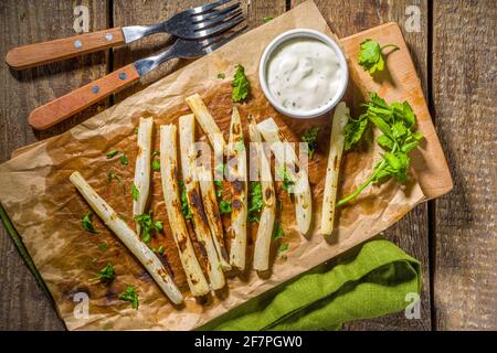 Gegrillter polnischer osteuropäischer schwarzer Spargel (schwarze Karotte) skorzonera, gekocht mit Gewürzen und Tsatziki-Sauce. Auf einem Holztisch Platz kopieren, Vegan Bar Stockfoto