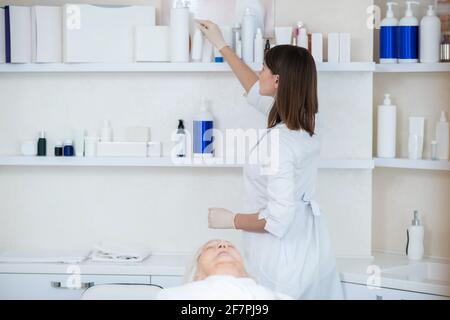 Kosmetologe in einem weißen Mantel, der Schönheitsprodukte aus der nimmt Regal Stockfoto