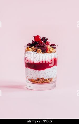 Nahaufnahme des Chia-Puddings mit Granola-Joghurt-Johannisbeeren in einem Transparentes Glas auf rosa Hintergrund Stockfoto