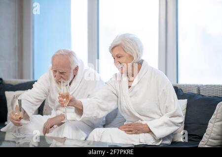 Das ältere Paar in weißen Bademänteln trank Champagner und sah zufrieden aus Stockfoto
