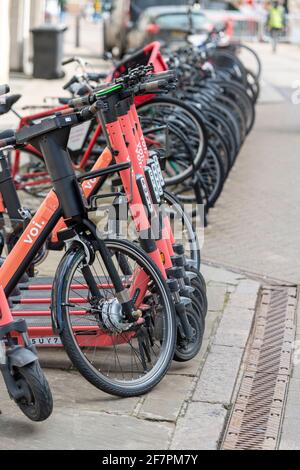 VOI-Elektrofahrräder und -Roller, die bei einer Sammlung geparkt sind Point for hire in Cambridge UK Stockfoto