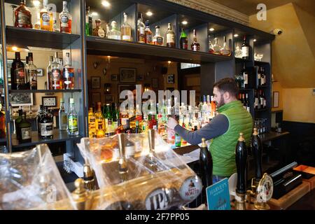 London, Großbritannien, 9. April 2021: Der Abbeville Pub in Clapham wird ab dem 12. April wieder für Drinks im Freien und zum Abendessen auf der Terrasse geöffnet. Während die Bierzapfhähne unter Plastikfolie sauber gehalten werden, stäubt Barkeeper Klodian Flaschen mit Spirituosen. Anna Watson/Alamy Live News Stockfoto
