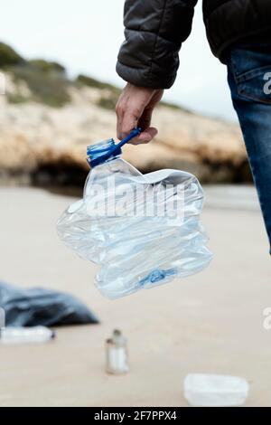 Ein junger Kaukasusmann sammelt eine gebrauchte Plastikflasche aus dem Sand eines einsamen Strandes, um die natürliche Umgebung zu reinigen Stockfoto