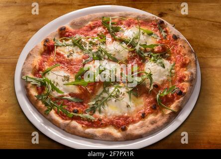 Pizza mit Rucola-Blättern, Tomatensauce, Mozzarella-Käse auf weißem Teller auf Holztisch, Draufsicht Stockfoto