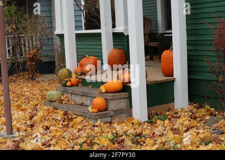 Ein knackiger Herbsttag mit gefallenen Blättern auf einem Rasen und einer mit Kürbissen geschmückten Veranda gibt Stimmung für kommende Halloween. Ländliche Amerika Stockfoto