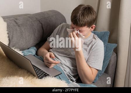 Teenager versucht, online zu lernen und niest in ein Papiertuch. Selbstisolierung. Quarantäne. E-learning über Entfernungen. Stockfoto