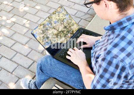 Junger Mann, der draußen auf einem Laptop tippt. Konzept des digitalen Nomaden, Arbeiten oder Studieren unter freiem Himmel. Stockfoto