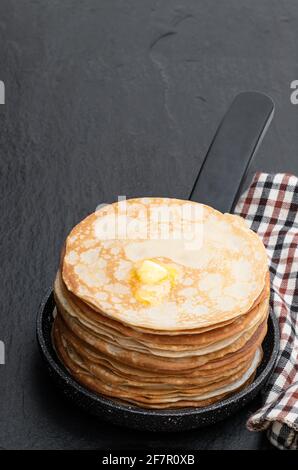 Stapel dünne Pfannkuchen in kleiner Pfanne auf schwarz Steinhintergrund Stockfoto