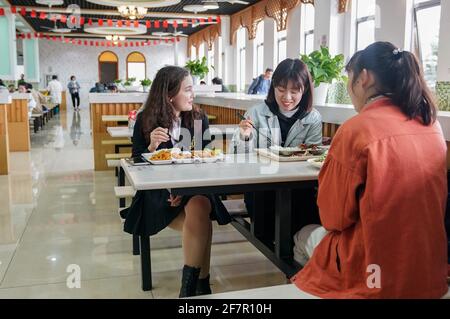 (210409) -- SHANGHAI, 9. April 2021 (Xinhua) -- Risalet Ehmet (L) hat eine Mahlzeit in einer Kantine in der Shanghai Lixin University of Accounting and Finance in Shanghai, Ostchina, 7. April 2021. Risalet Ehmet, 19, stammt aus dem Bezirk Zepu in Kashgar, nordwestlich der Autonomen Region Xinjiang Uygur in China. Heute studiert sie an der School of Information Management der Shanghai Lixin University of Accounting and Finance. Mit Hilfe von Lehrern und Mitschülern passte sie sich schnell an das Universitätsleben an. „nach dem Studium werde ich das Gelernte einsetzen, um die Spezialitäten aus meinem Haus zu fördern Stockfoto