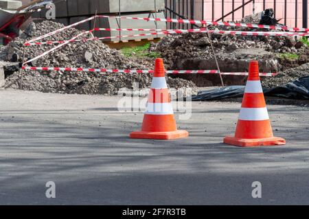 Leuchtend orangefarbene Verkehrskegel stehen in einer Reihe auf dunklem Asphalt. Loch auf der Straße mit einem orangefarbenen Kegel. Stockfoto