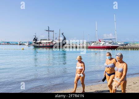 Wikingerboot im Hafen und drei Frauen zu Fuß am Strand von Los Cristianos, Teneriffa, Kanarische Inseln, Spanien Stockfoto