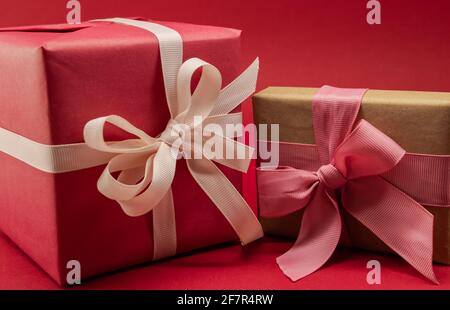 Zwei Schachteln in verschiedenen Größen mit Geschenken für den Urlaub auf rotem Hintergrund, in Papier gewickelt und mit Bändern gebunden Stockfoto