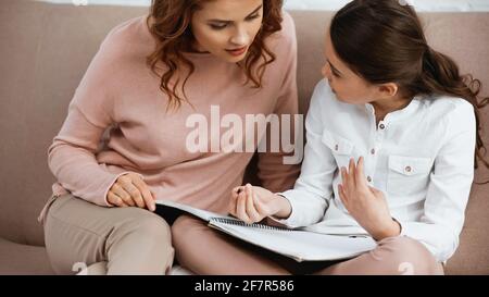 Frau hilft Tochter mit Stift und Notizbuch während der Ausbildung zu Hause Stockfoto