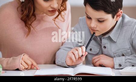 Mutter, die neben dem Kind sitzt und mit dem Stift Hausaufgaben macht Stockfoto