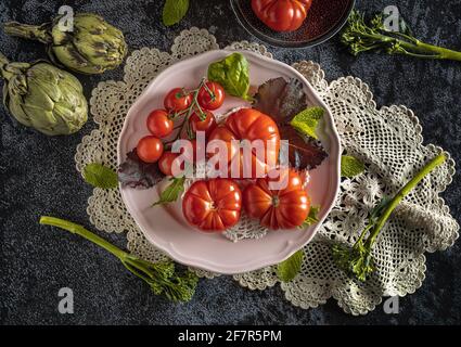 Moody Dark Food Fotografie von frischen raf Tomaten, Bimi und Artischocken. Flaches Standbild mit Vintage-Look und schwarzem Hintergrund. Stockfoto