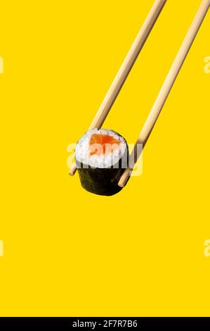 Nahaufnahme Maki Roll mit Lachsfisch auf Essstäbchen auf gelbem Hintergrund. Stockfoto