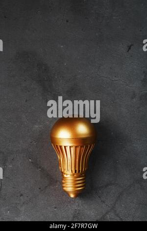 Goldene Glühbirne auf einem schwarzen strukturierten Hintergrund. Das Konzept der Idee. Freier Speicherplatz, Draufsicht Stockfoto