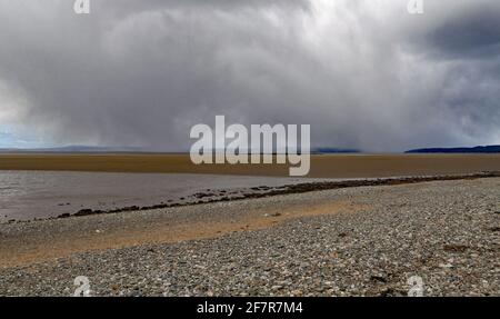 An einem Frühlingstag fällt Schnee über den Sand- und Kies- und Steinstrand der Morecambe Bay vor der Nordwestküste Englands, Blick von der HEST Bank. Stockfoto