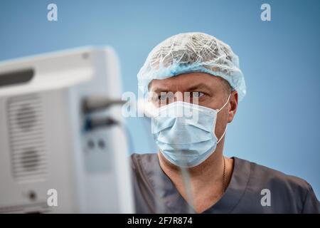 Anästhesist, der während der Herzoperation die lebenswichtigen Funktionen des Körpers verfolgt. Chirurg, der während der Operation einen medizinischen Monitor ansieht. Doktor Checki Stockfoto