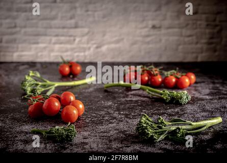 Food-Fotografie von frischen Kirschtomaten und Bimi auf einem Steintisch mit Ziegelwand. Standbild mit einem Kopierbereich. Stockfoto