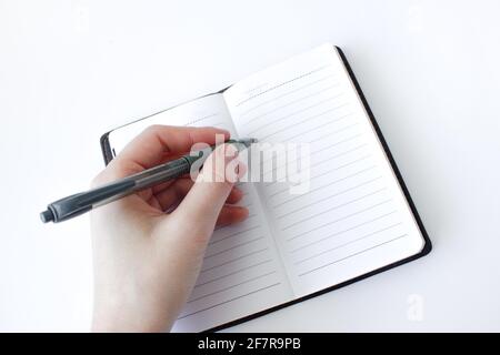 Frau Hand schreibt auf einem Notizbuch mit einem Stift auf weißem Hintergrund. Draufsicht Stockfoto