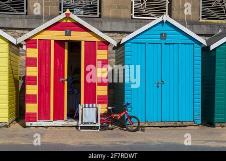 Kinder rotes Fahrrad und Klappstuhl vor bunten Strandhütten in Boscombe, Bournemouth, Dorset UK im April Stockfoto