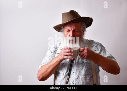 Älterer kaukasischer bärtiger Mann, der seinen Kaffee zum Abkühlen aufbläst Es ist aus Stockfoto