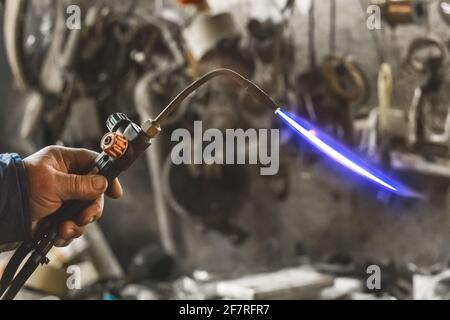 Gasbrenner mit brennender Flamme aus der Nähe auf dem Hintergrund einer Industriewerkstatt. Stockfoto