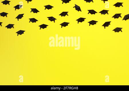 Abschlussmützen Konfetti auf gelbem Hintergrund. Hintergrund der Feier. Stockfoto