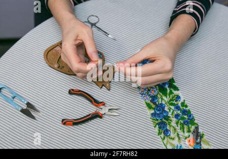 Weben aus Perlen. Nahaufnahme - die Hände einer Frau ziehen Perlen an einen Faden und machen Schmuck. Die Frau webt gern aus Perlen. Stockfoto