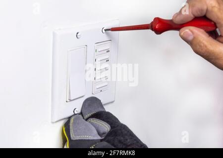 Der Elektriker bereitete die Schrauben zur Befestigung der Schalterabdeckung vor und führte sie in die Löcher ein und hielt sie mit einem Schraubendreher fest. Stockfoto