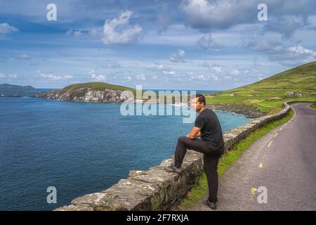 Mann im mittleren Alter, der den atemberaubenden Blick auf Slea Head, Coumeenoole Beach und die Halbinsel Dingle, Teil des Wild Atlantic Way, Kerry, Irland, beobachtet und bewundert Stockfoto